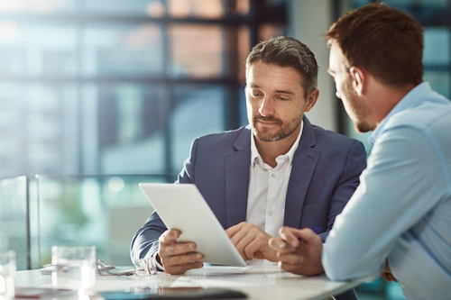 Two business professionals discussing information on a tablet in a modern office setting.