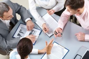 Business professionals collaborating on IT consulting and project management, reviewing strategic plans, analyzing data, and discussing technology solutions to align with organizational goals.