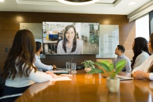 Business team in a conference room participating in a video call with a remote colleague.