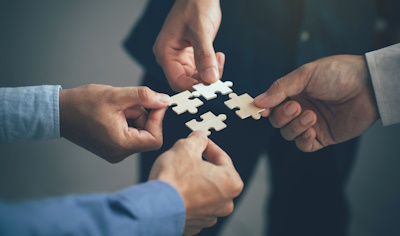 Four hands holding puzzle pieces, symbolizing teamwork, collaboration, and problem-solving.